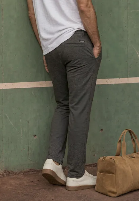 Mann trägt dunkelgraue Hose und weiße Sneaker, daneben steht eine Reisetasche.