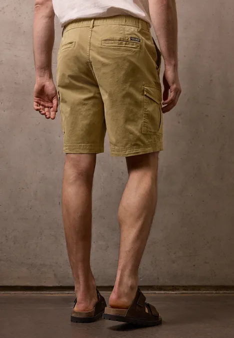 Ein Mann von hinten in khakifarbenen Shorts und Sandalen vor einer neutralen Wand.