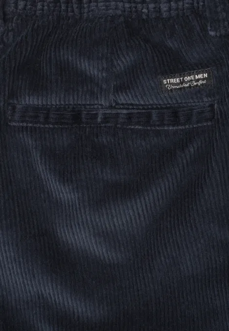 Gros plan sur un pantalon en velours côtelé bleu foncé avec couture apparente et petit logo.