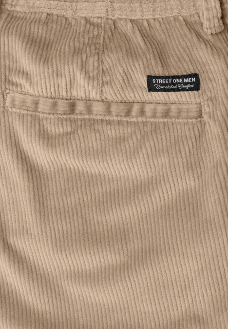 Gros plan sur un tissu velours côtelé beige, pochette et petite étiquette noire à la taille.