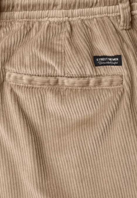Gros plan d'un pantalon en velours côtelé beige avec poche arrière et petit label noir 'STREET MOTOR'.