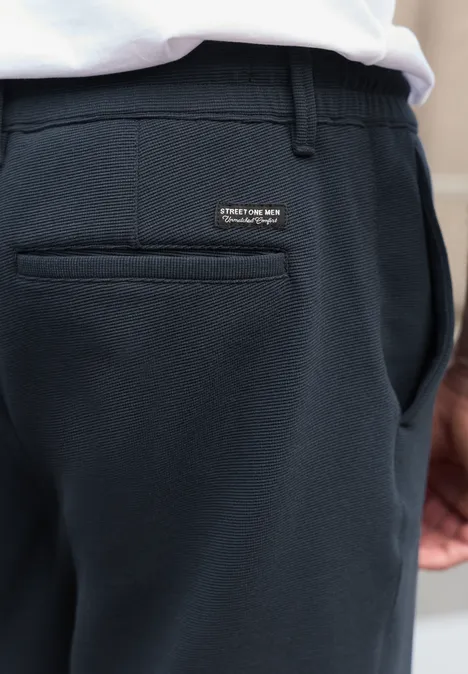 Gros plan sur un pantalon bleu foncé avec poche arrière et petit logo, un t-shirt blanc visible.