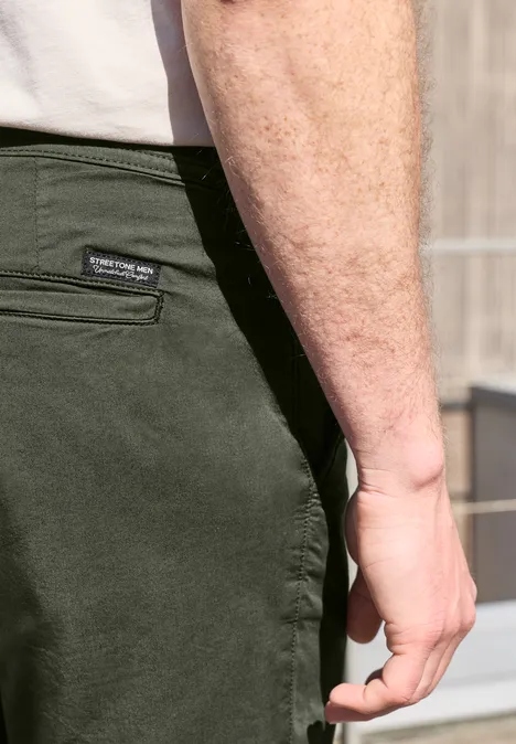 Nahaufnahme eines Mannes in olivgrüner Hose und weißem T-Shirt, Fokus auf Hand und Hüfte.