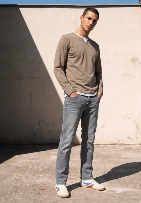 Straight Leg Jeans im Regular Fit mid grey random wash Ein sportlicher Mann in beigem Pullover, grauer Jeans und bunten Sneakern steht entspannt an einer sonnigen Wand.