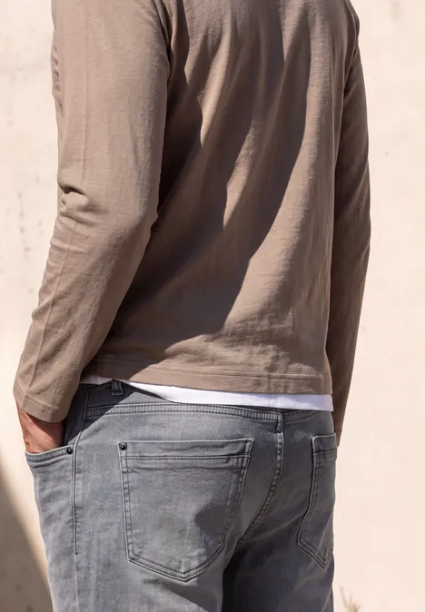 Straight Leg Jeans im Regular Fit mid grey random wash Mann von hinten in grauer Jeans und beigem Langarmshirt, vor einer hellen Wand.