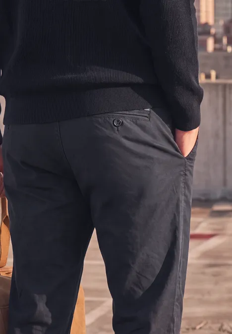 Nahaufnahme eines Mannes von hinten in dunkelgrauen Hosen mit Händen in den Taschen auf einem Dach