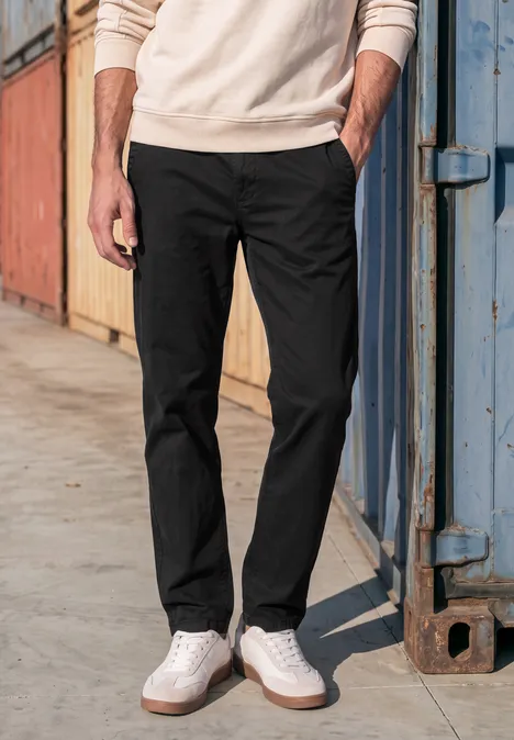 Slim Leg chino met flexibele tailleband basic black Onderlichaam van een man in zwarte broek en witte sneakers voor kleurrijke containers.