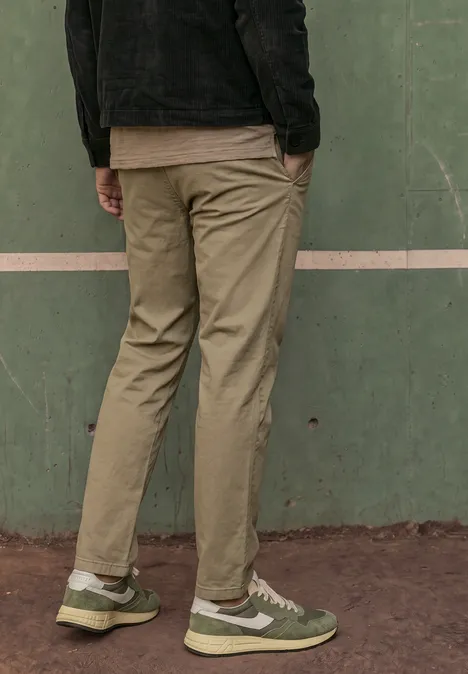 Persoon staat voor een groene muur en draagt olijfgroene broek en groene sneakers.