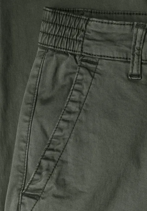 Close-up van een donkergroene broek met elastische taille, riemlussen en zijzak.
