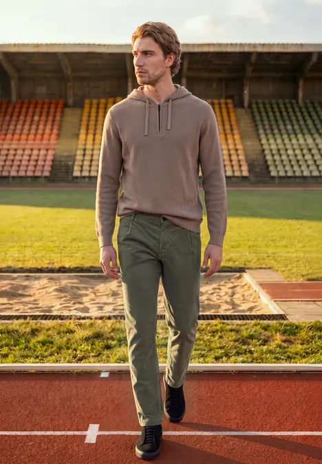 Homme en tenue décontractée marche sur une piste d’athlétisme devant des gradins vides.