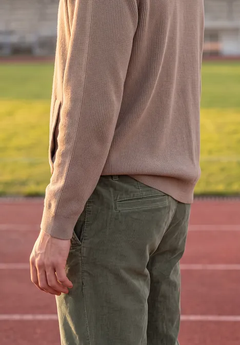 Personne en pull beige et pantalon vert debout sur une piste d’athlétisme.