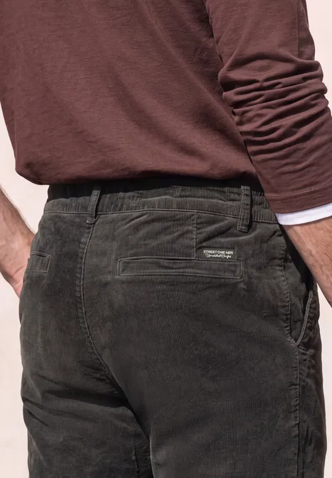Pantalon chino en velours côtelé avec plis marqués au fer à repasser obsidian grey Homme vu de dos portant un pantalon en velours côtelé vert foncé et un t-shirt à manches longues marron.