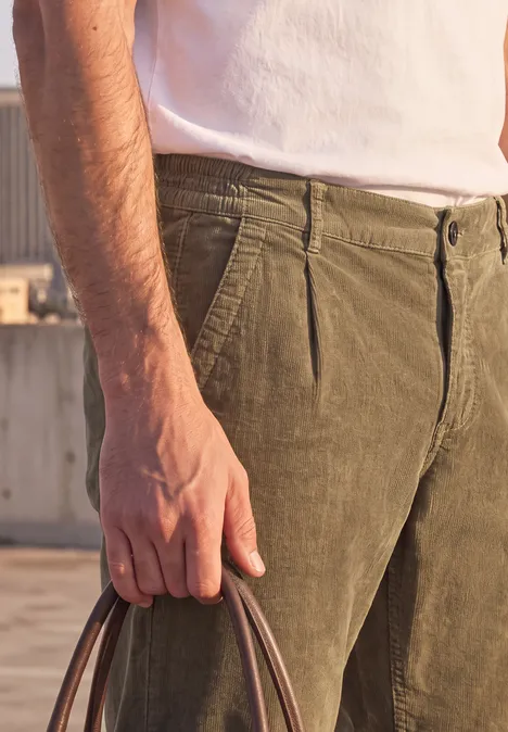 Pantalon chino en velours côtelé avec plis marqués au fer brass brown Gros plan d’une personne en t-shirt blanc et pantalon olive, tenant un sac à la main.