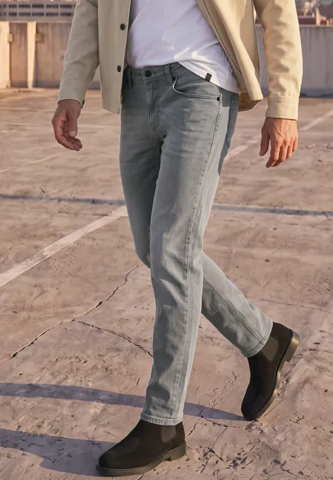 Slim Leg Jeans im Slim Fit mid grey random wash Ein Mann in grauer Jeans, beigem Sakko und schwarzen Stiefeln geht über einen Betonboden.