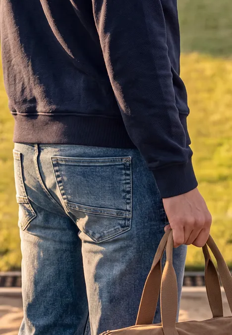 Eine Person in Jeans und Kapuzenpullover steht von hinten und hält eine Tasche in der Hand.