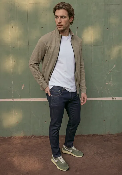 Een man in casual kleding staat op een tennisbaan voor een groene muur.