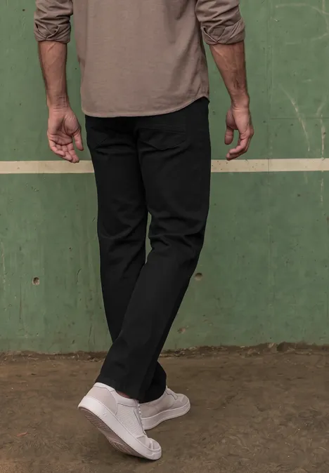 Onderlichaam van een persoon met zwarte broek en witte sneakers voor een groene muur.