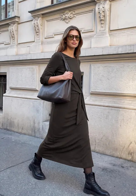 Midikleid aus Jersey mit Knotendetail charred brown Stylische Frau in langem schwarzen Kleid und Stiefeln läuft selbstbewusst eine Straße entlang.