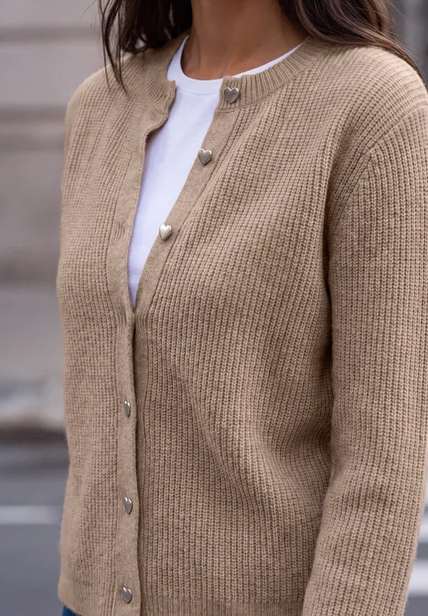 Person trägt eine beige Strickjacke mit Knöpfen über weißem Oberteil