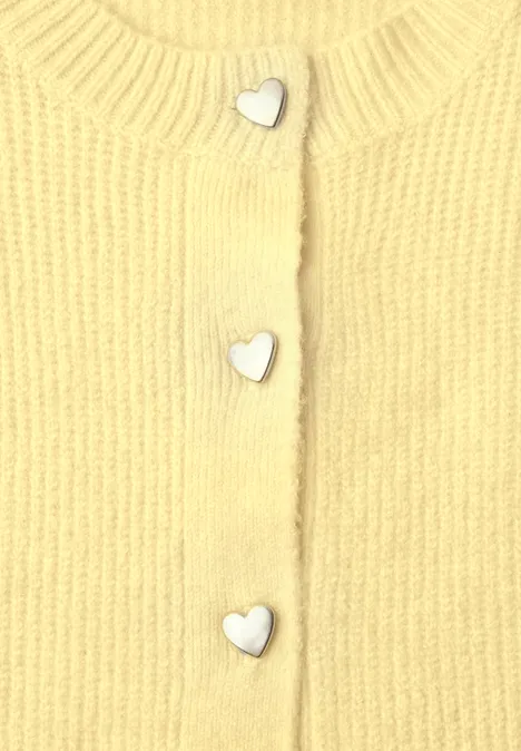 Nahaufnahme eines gelben Strickoberteils mit silbernen herzförmigen Knöpfen.