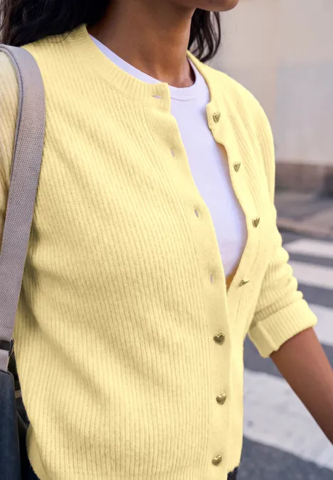 Eine Frau trägt eine gelbe Strickjacke über einem weißen Shirt.