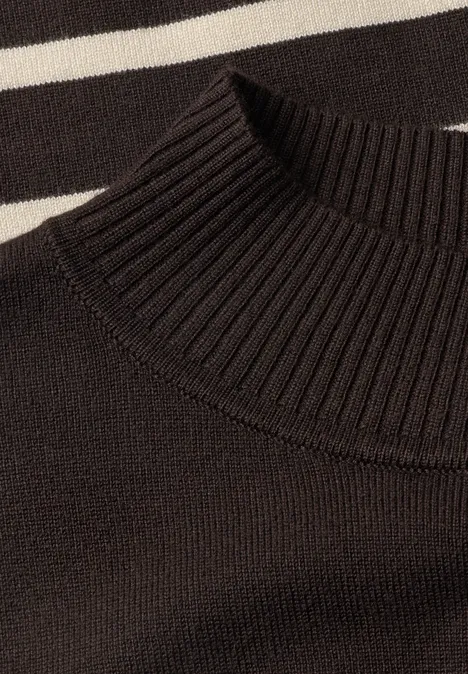 Schwarzer Rollkragenpullover mit geripptem Strickmuster, vor weiß-schwarz gestreiftem Hintergrund.