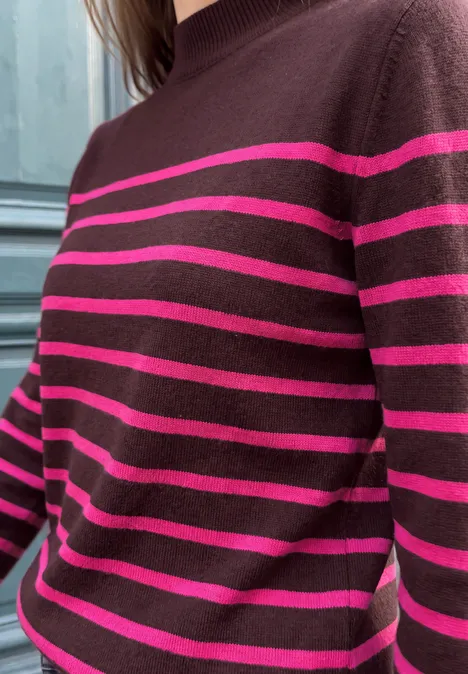 Eine Person trägt einen dunkelbraunen Pullover mit auffälligen pinken Querstreifen.