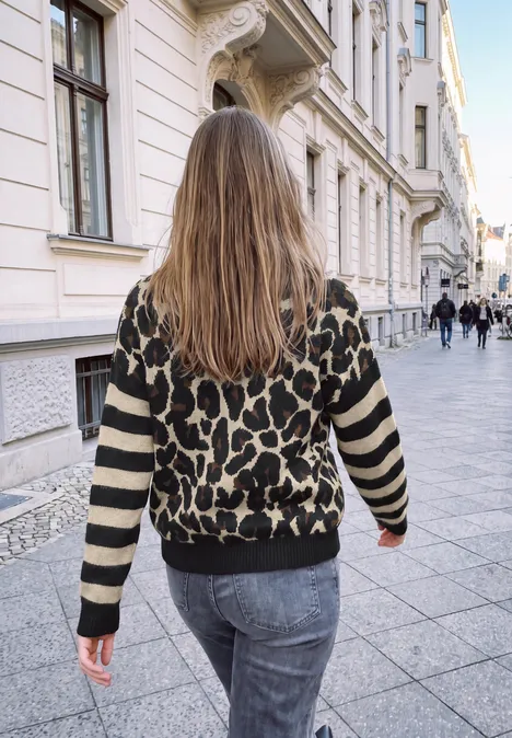 Trui met luipaardprint en gestreepte mouwen Black Frau mit langem Haar und Leopardenpullover spaziert durch eine elegante, städtische Gasse.