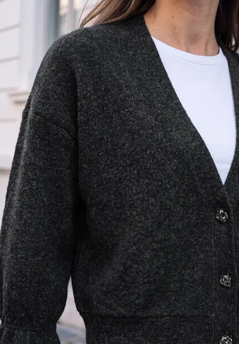 Une femme porte un gilet gris foncé sur un t-shirt blanc.