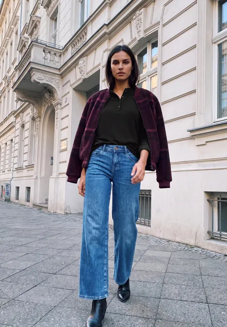 Shirt met lange mouwen, ronde hals en ruches Black Eine Frau in weiten Jeans, schwarzem Shirt und karierter Jacke geht an einer Altbau-Fassade vorbei.