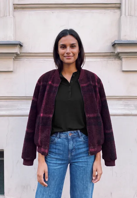 Shirt met lange mouwen, ronde hals en ruches Black Eine Frau in Jeans, schwarzem Shirt und weinrotem Karomantel steht vor einer hellen Hauswand.