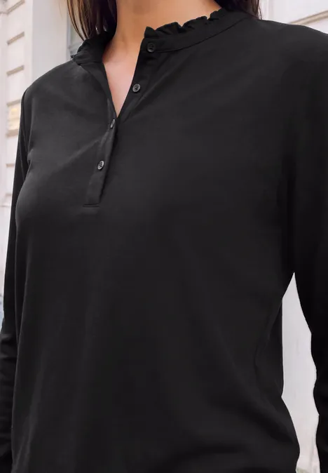 Shirt met lange mouwen, ronde hals en ruches Black Schwarzlangärmeliges Henley-Shirt mit Rüschenkragen, Knopfleiste und schmaler Passform vor hellem Hintergrund.