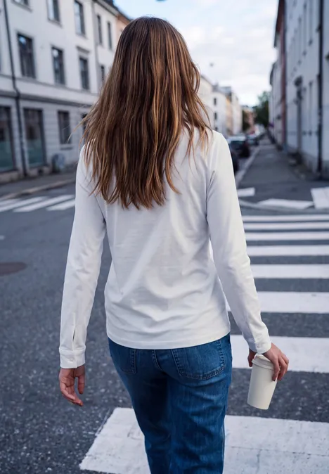 Shirt met lange mouwen, ronde hals en ruches off white Eine Frau mit weißem Langarmshirt, blauen Jeans und braunen Haaren hält einen Coffee-to-go-Becher auf einem Zebrastreifen.