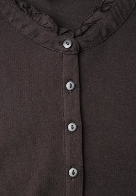 Shirt met lange mouwen, ronde hals en ruches charred brown Nahaufnahme eines braunen Oberteils mit Rüschen am Kragen und fünf grauen Knöpfen.