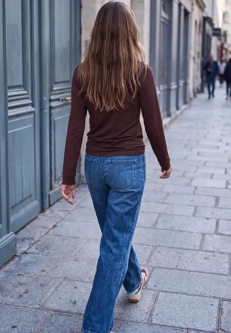 Shirt met lange mouwen, ronde hals en ruches russet red Eine Frau in Jeans und braunem Oberteil geht eine gepflasterte Straße entlang, aufgenommen von hinten.