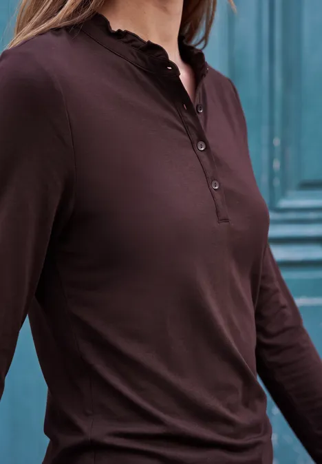 Shirt met lange mouwen, ronde hals en ruches russet red Eine Frau trägt ein braunes Langarm-Henleyshirt mit Knopfleiste vor einer türkisfarbenen Wand.