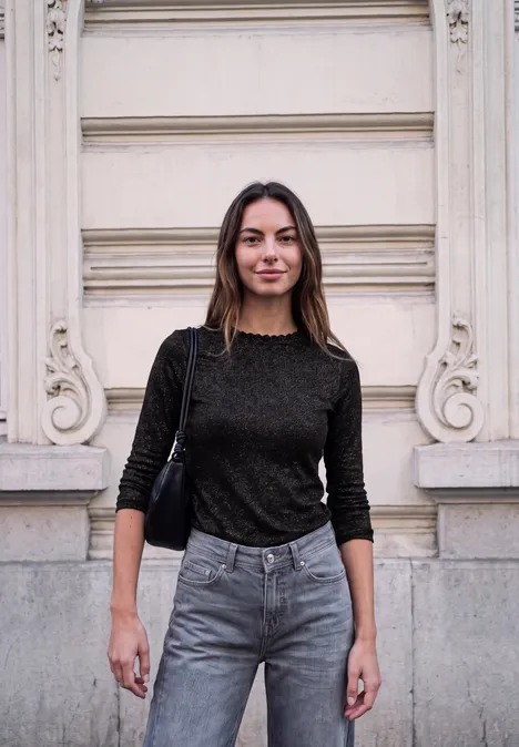 Shirt met lange mouwen, ronde hals en ruches Black Eine Frau in schwarzem Pullover und Jeans steht vor einer hellen Fassade und blickt in die Kamera.