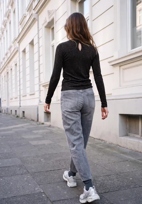 Shirt met lange mouwen, ronde hals en ruches Black Eine Frau in schwarzem Pullover und grauer Jeans spaziert an einer weißen Häuserfassade entlang.