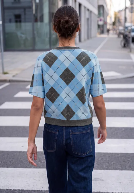 Shirt met gebreide look en argylepatroon loom blue Frau in blauem Rautenmuster-Pullover und Jeans steht auf einem Zebrastreifen in der Stadt.