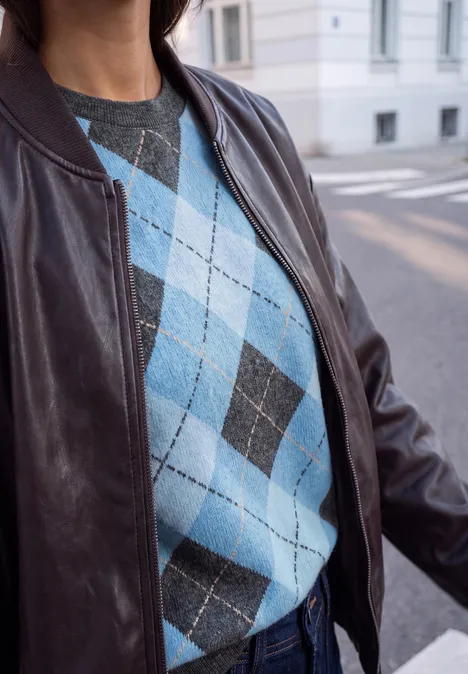 Shirt met gebreide look en argylepatroon loom blue Im Bild ist eine Person mit blau-grauem Rautenmuster-Pullover und brauner Lederjacke auf der Straße.