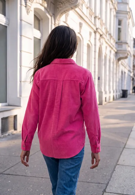Eine Frau in rosa Bluse und Jeans läuft auf einem Bürgersteig entlang weißer Altbauhäuser.