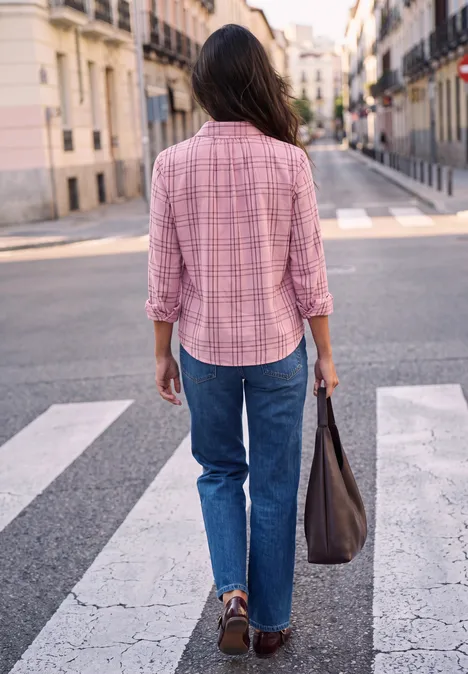 Eine Person in rosa Hemd und Jeans überquert einen Zebrastreifen und trägt eine Tasche.