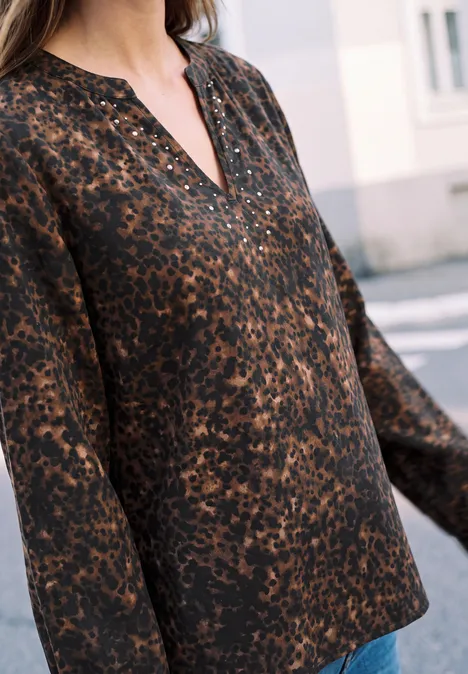 Tunique à col fendu et détails rivetés charred brown Gros plan sur une femme portant un chemisier à manches longues motif léopard marron et encolure en V devant un bâtiment.