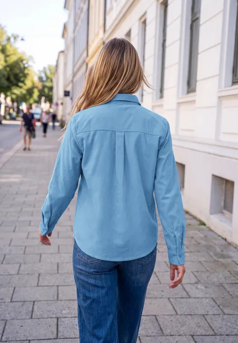 Frau von hinten in Jeanshemd und Jeans spaziert auf städtischem Gehweg.
