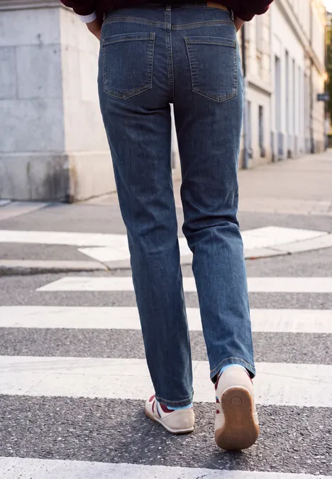 Hinteransicht einer Person in blauen Jeans und Turnschuhen, die über einen Zebrastreifen läuft.