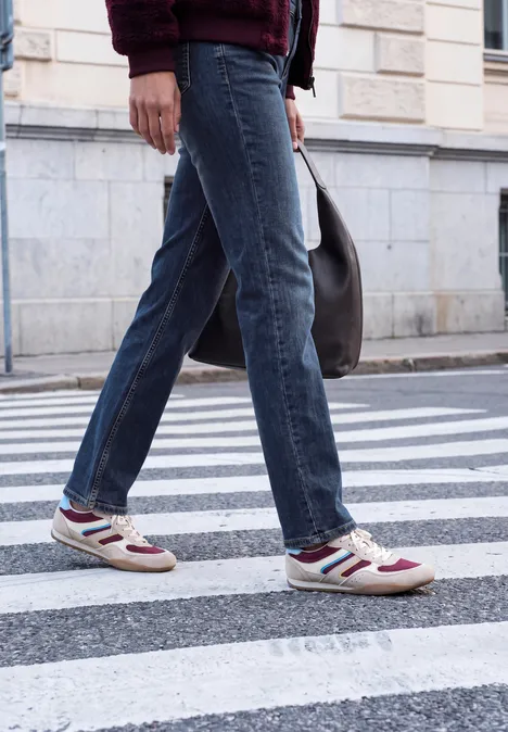 Person in Jeans und Sneakern überquert einen Zebrastreifen auf der Straße.