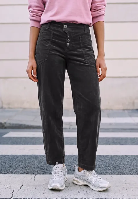 Personne debout sur le trottoir portant un pantalon en velours côtelé noir et des baskets blanches