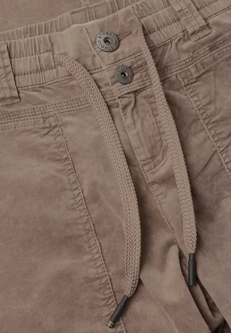 Nahaufnahme einer braunen Cordhose mit Bündchen, Kordelzug, Taschen und Metallknöpfen.
