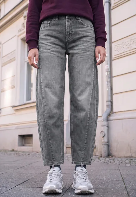 Relaxed Barrel Leg Jeans im Loose Fit grey authentic washed Unterkörper einer Person in grauen Jeans und weißen Sneakern auf Bürgersteig vor einer Hauswand.