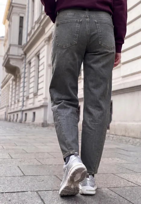 Relaxed Barrel Leg Jeans im Loose Fit grey authentic washed Eine Person in grauen Jeans und weißen Sneakers geht auf Kopfsteinpflaster an einem alten Gebäude entlang.